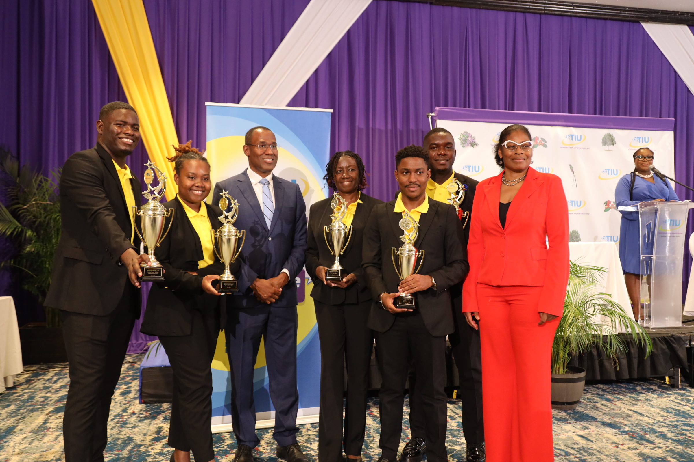 Minister of Finance and the Public Service, Hon. Nigel Clarke (3rd left) and Executive Director of the Transformation Implementation Unit Maria Thompson Walters (right) presents trophies to members of the MoJ Debate Team – (from left – right): Demoye Whiteley, Joanalee Robertson, Claudia Powell, Payton Patterson and Oschain Haynes.